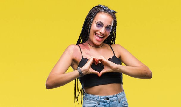 Young braided hair african american with birth mark wearing sunglasses over isolated background smiling in love showing heart symbol and shape with hands. Romantic concept. - Foto, immagini