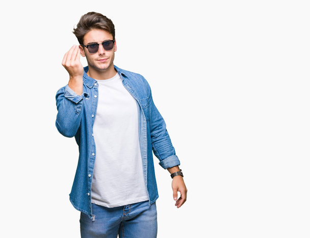 Jovem homem bonito usando óculos de sol sobre fundo isolado Fazendo gesto italiano com mão e dedos expressão confiante
 - Foto, Imagem