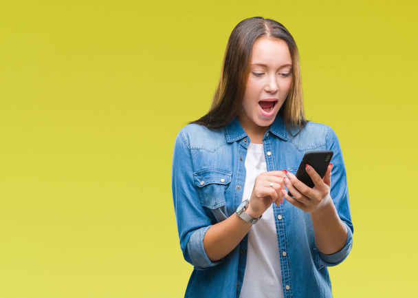 Young beautiful caucasian woman texting sending message using smartphone over isolated background scared in shock with a surprise face, afraid and excited with fear expression - Photo, image