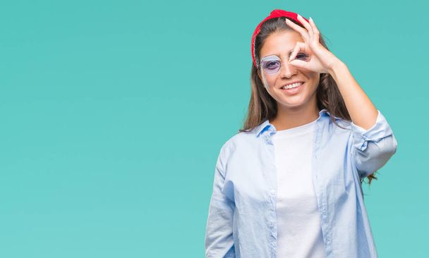 junge schöne arabische Frau mit Sonnenbrille über isoliertem Hintergrund tut ok Geste mit der Hand lächelnd, Blick durch die Finger mit glücklichem Gesicht. - Foto, Bild