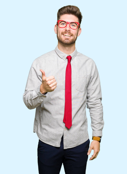 Молодой привлекательный бизнесмен в очках делает счастливый жест вверх рукой. Утверждение выражения лица, смотрящего в камеру с успехом
. - Фото, изображение