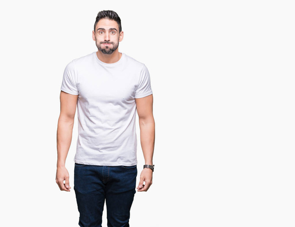 Hombre joven con camiseta blanca casual sobre fondo aislado hinchando mejillas con cara divertida. Boca hinchada con aire, expresión loca
. - Foto, imagen