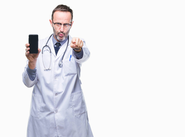 Старший седовласый врач средних лет показывает экран смартфона на изолированном фоне, указывая пальцем на камеру и на вас, знак руки, позитивный и уверенный жест спереди
 - Фото, изображение