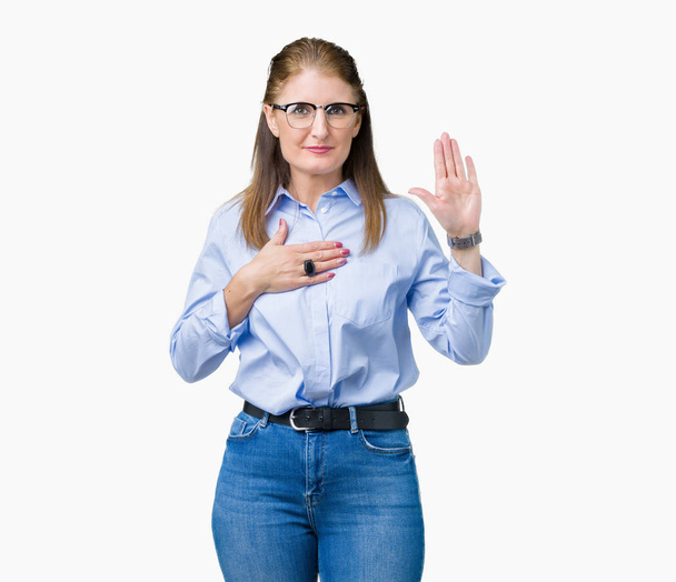 Bella donna d'affari matura di mezza età che indossa occhiali su sfondo isolato giurando con mano sul petto e palmo aperto, facendo un giuramento di fedeltà
 - Foto, immagini