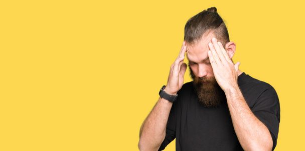 Blonde jongeman casual t-shirt met de hand dragen op hoofd voor pijn in hoofd, omdat stress. Lijden van migraine. - Foto, afbeelding