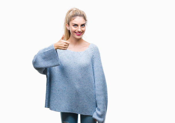 Νέα όμορφη ξανθιά και μπλε μάτια γυναίκα φορώντας χειμωνιάτικο πουλόβερ πάνω από απομονωμένο φόντο κάνει ευτυχισμένο αντίχειρες προς τα πάνω χειρονομία με το χέρι. Έγκριση έκφρασης κοιτάζοντας την κάμερα με εμφάνιση επιτυχίας. - Φωτογραφία, εικόνα