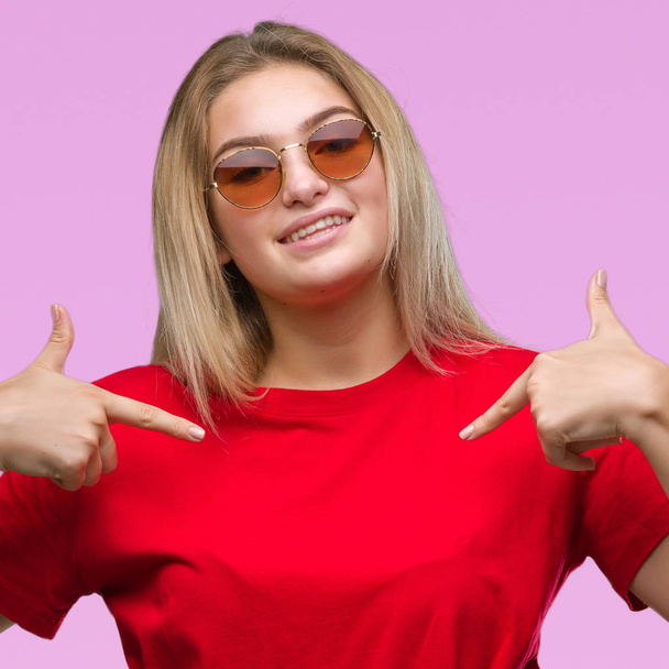Young caucasian woman wearing sunglasses over isolated background looking confident with smile on face, pointing oneself with fingers proud and happy. - Foto, Imagem