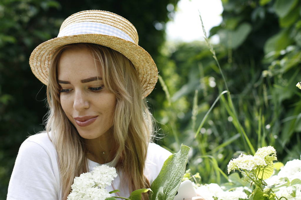 Girl blonde in a straw hat in the park on a background of white flowers - Photo, Image