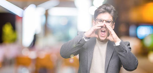 Молодой бизнесмен в очках на изолированном фоне кричит громко, с руками над ртом
 - Фото, изображение