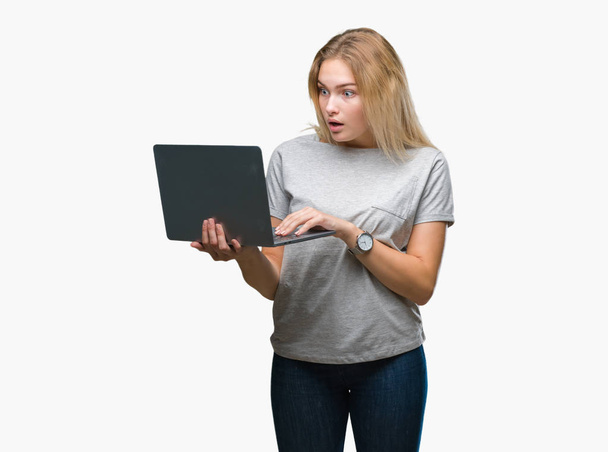 Jonge Kaukasische vrouw met behulp van computer laptop over geïsoleerde achtergrond bang in schok met een verrassing gezicht, bang en opgewonden met angst expressie - Foto, afbeelding