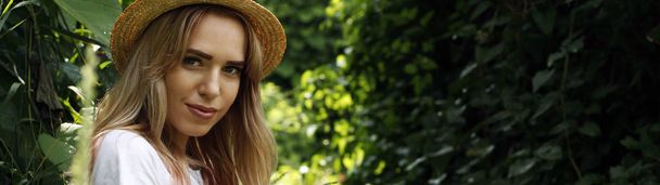 A girl with a piercing gaze in a straw hat on a green park background - Photo, Image