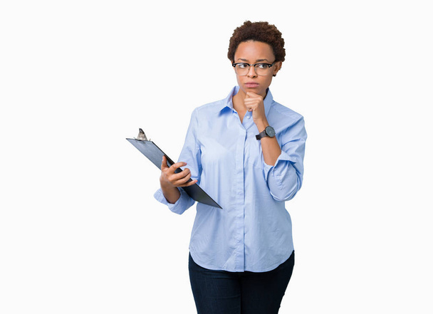 Young african american businesss woman holding clipboard over isolated background serious face thinking about question, very confused idea - Foto, Imagem