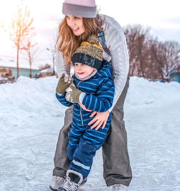 Girl hold a little boy. In winter, city skate. Front view. Sister with her son learns to skate and stand on skates. - Фото, изображение