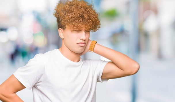Młody przystojny mężczyzna z afro włosów, noszenia na co dzień biały t-shirt cierpienia urazu ból szyi, dotykając karku z ręki, bóle mięśni - Zdjęcie, obraz