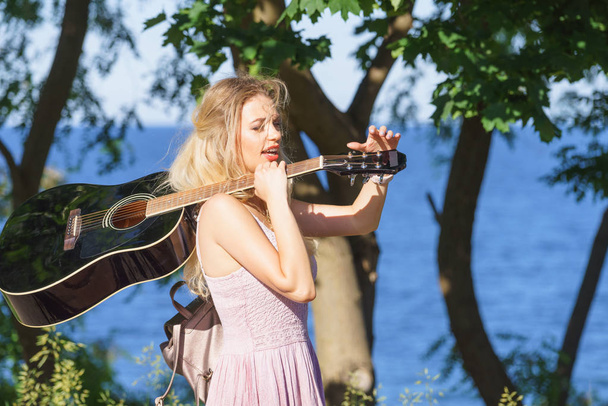 Hippie looking young adult woman wearing gypsy outfit having acoustic guitar. Female playing music in park. - Foto, imagen