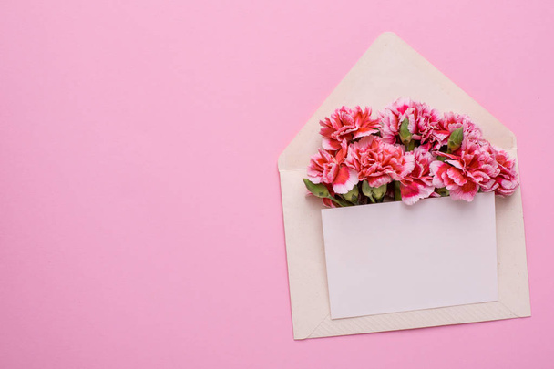 An envelope with pink flowers and a present card on a pink background top view - Foto, afbeelding