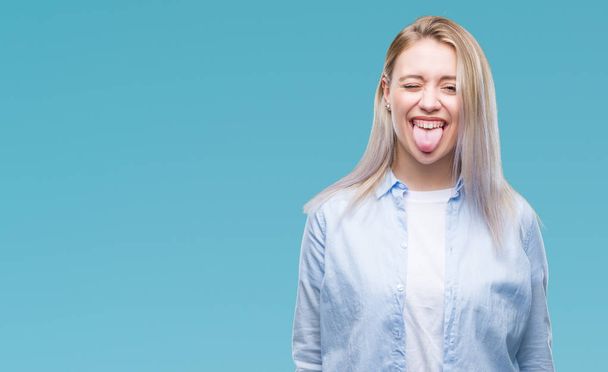 junge blonde Frau über isoliertem Hintergrund streckt die Zunge glücklich mit lustigem Ausdruck heraus. Emotionales Konzept. - Foto, Bild