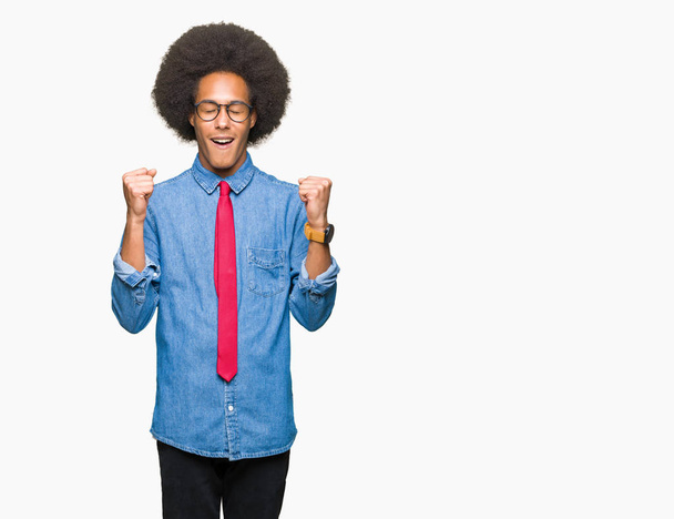 Young african american business man with afro hair wearing glasses and red tie excited for success with arms raised celebrating victory smiling. Winner concept. - Photo, Image