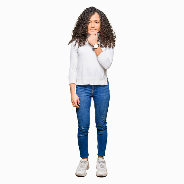 Young beautiful woman with curly hair wearing turtleneck sweater looking confident at the camera with smile with crossed arms and hand raised on chin. Thinking positive. - Fotó, kép