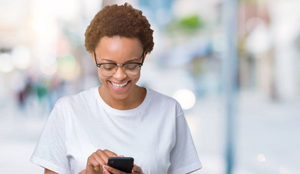 Nuori afrikkalainen amerikkalainen nainen, joka käyttää älypuhelinta eristetyn taustan yli iloisella kasvolla seisoen ja hymyillen luottavaisesti hymyillen.
 - Valokuva, kuva