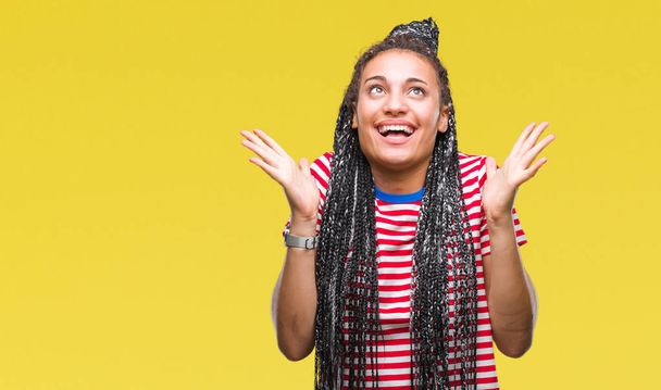 Young braided hair african american girl over isolated background celebrating crazy and amazed for success with arms raised and open eyes screaming excited. Winner concept - Photo, Image