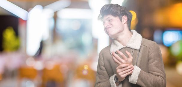 Όμορφος νεαρός φοράει παλτό χειμώνα πάνω από απομονωμένες φόντο πόνο πόνο στα χέρια και τα δάχτυλα, αρθρίτιδα φλεγμονή - Φωτογραφία, εικόνα