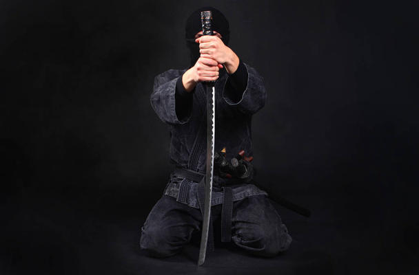 Ninja samurai warrior sits on his knees and covers his face with a sword. Anonymity and confidentiality concept.  - 写真・画像