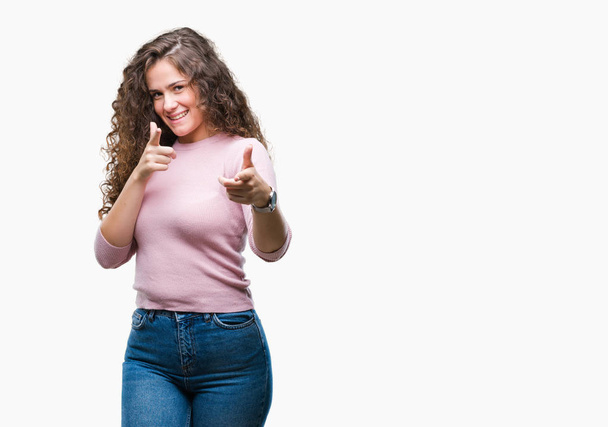 Beautiful brunette curly hair young girl wearing pink sweater over isolated background pointing fingers to camera with happy and funny face. Good energy and vibes. - Φωτογραφία, εικόνα
