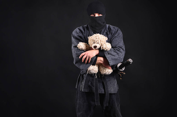 Big and powerful ninja samurai holding a teddy bear. Good and strength. Protection of the weak concept. - Фото, изображение