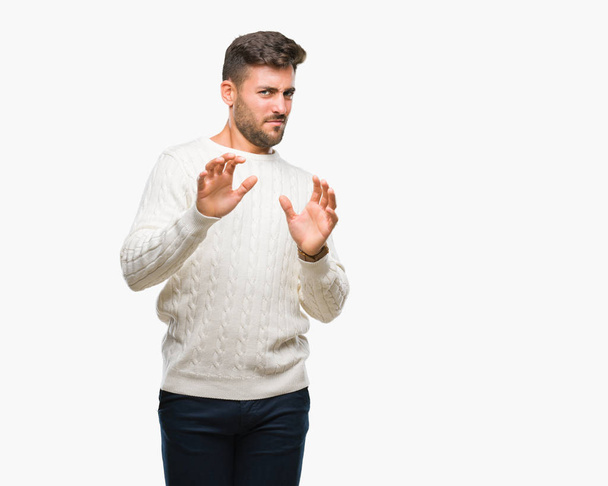 Young handsome man wearing winter sweater over isolated background disgusted expression, displeased and fearful doing disgust face because aversion reaction. With hands raised. Annoying concept. - Photo, Image