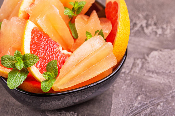 Домашнее грейпфрутовое мороженое со спелыми ломтиками грейпфрута и свежей мятой на темно-бетонном фоне. Здоровые десерты. Мороженое без лактозы
 - Фото, изображение