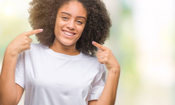 Giovane donna afro-americana su sfondo isolato sorridente fiducioso mostrando e indicando con i denti delle dita e della bocca. Concetto sanitario
. - Foto, immagini