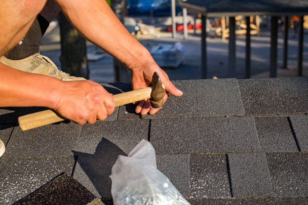 Workers hands installing bitumen roof shingles using hammer in nails. - Фото, изображение