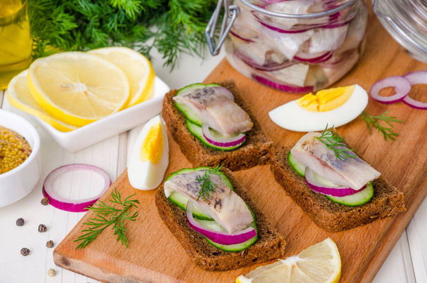 Open sandwich with rye bread, fresh cucumber, pickled onions, herring and dill on a wooden board - Zdjęcie, obraz