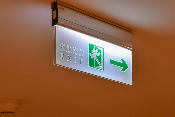 Primer plano de señal de salida de emergencia escribir en chino e inglés palabra en el techo dentro del centro comercial
 - Foto, imagen