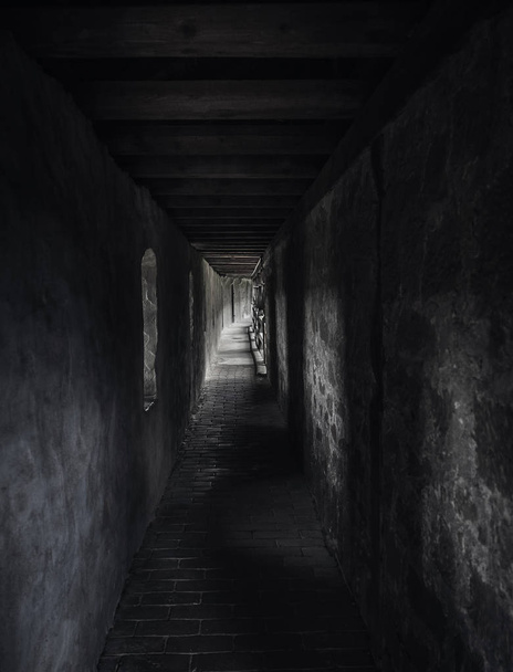 Passage altéré par faible luminosité, dans un bâtiment médiéval, avec des rayons de lumière. Un long couloir dans l'ombre avec de la lumière à la fin. Architecture vintage
. - Photo, image