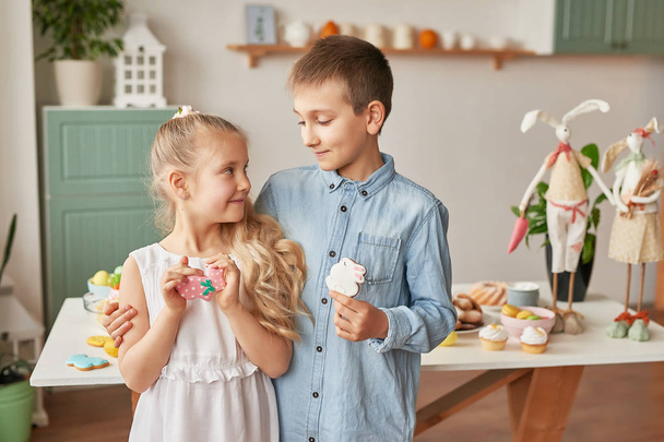 kids in the kitchen on easter day, boy and girl with easter gingerbread and eggs - Foto, Bild