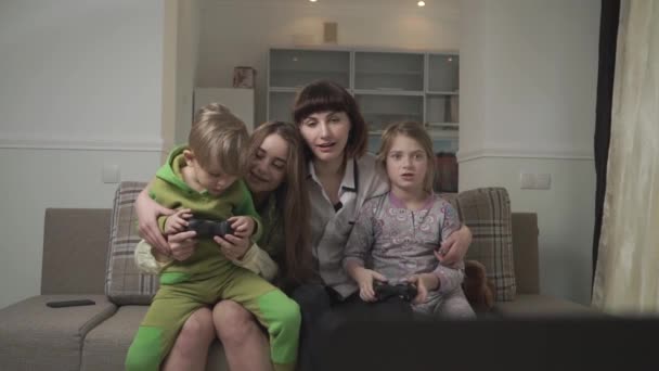 Happy older sisters and joyful younger kids sitting on the couch playing video games in the guest room. Fun family holiday. - Кадри, відео