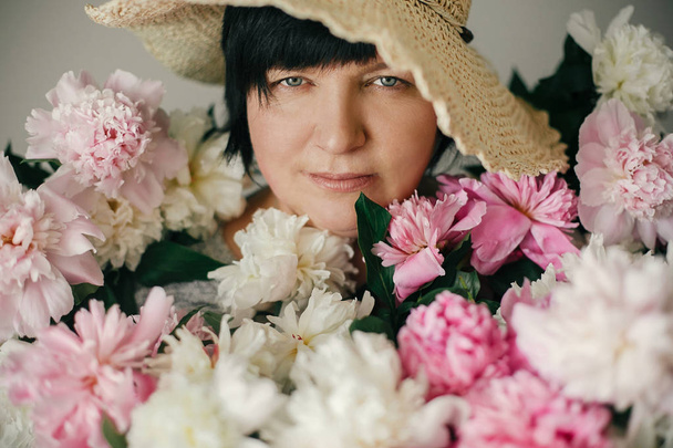 Happy mother with big bouquet of pink peonies giving from children. Happy Mothers day concept. Beautiful elder woman in hat posing with many peony flowers. International Womens Day - Photo, Image