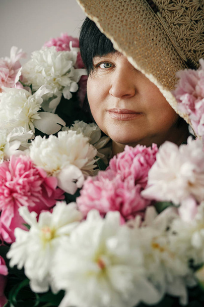 Beautiful woman in hat posing with many peony flowers. Happy mother with big bouquet of pink peonies from children. Happy Mothers day concept. International Womens Day - Photo, Image