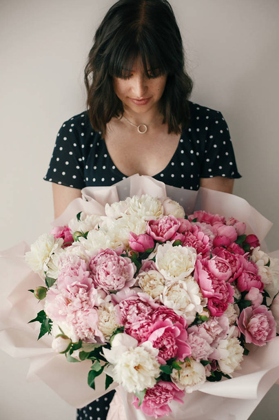 Belle fille brune en robe vintage tenant un grand bouquet avec des pivoines roses et blanches. Heureuse femme élégante avec des fleurs de pivoine dans la chambre. Journée internationale de la femme
 - Photo, image