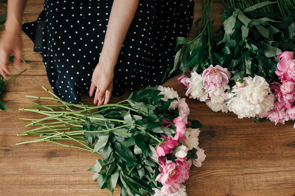 Beautiful girl in vintage dress holding scissors and cutting stems of pink and white peonies. Happy stylish woman arranging peony flowers in room. Florist in studio. Womens Day - Foto, imagen