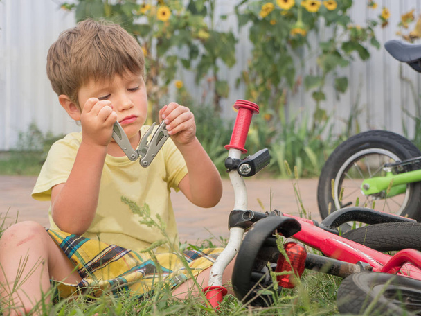 Boy fixing bicycle. Front, back yard background. Transport and children. Cycle on the grass. Happy childhood concept. Boy playing outside. Summer holidays background. Repair of bicycles background. - Zdjęcie, obraz