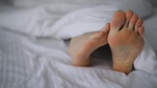 Calentamiento de los pies masculinos en la cama bajo la manta
 - Metraje, vídeo