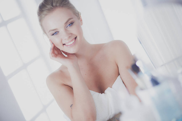 Young woman in bathrobe looking in bathroom mirror - Foto, Imagen