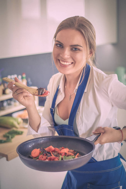 Young woman standing by the stove in the kitchen - Foto, Bild
