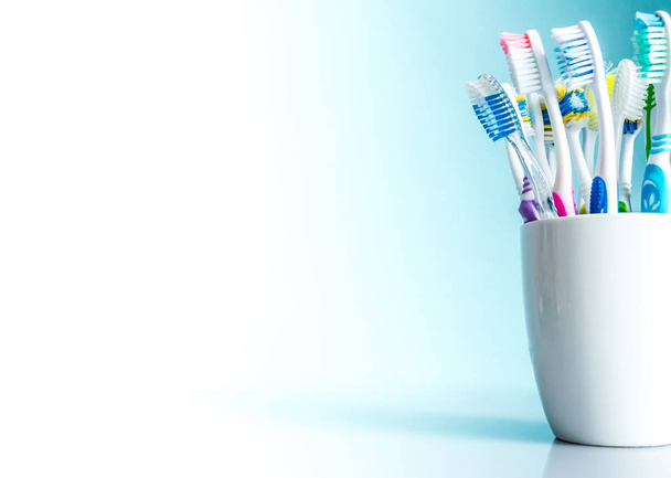 Multi-colored toothbrushes in a white mug close-up with a gradient background from white to blue with an isolated place for text - Φωτογραφία, εικόνα