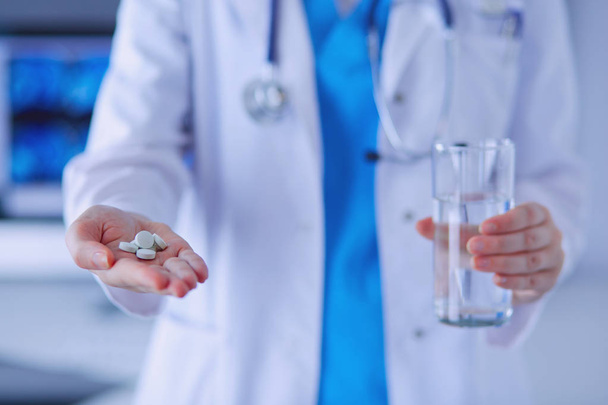 shot of doctors hands holding pills and glass of water at clinic. - Photo, image
