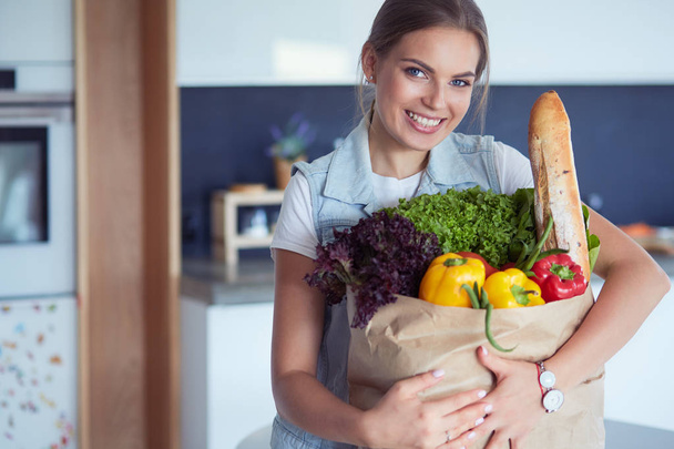 Young woman holding grocery shopping bag with vegetables .Standing in the kitchen - Valokuva, kuva