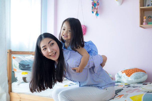 feliz poco asiático chica en la espalda de su madre en la casa
 - Foto, Imagen
